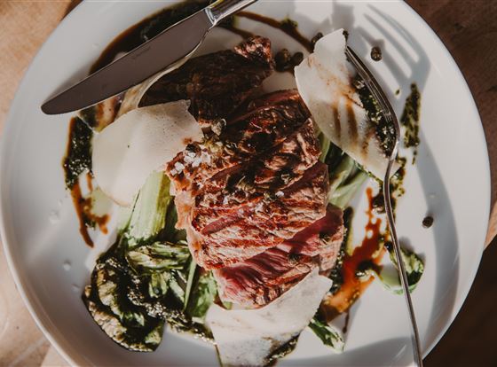 Ein ansprechend angerichteter Teller mit gebratenem Fleisch, begleitet von frischem Gemüse und einer feinen Sauce. Die Präsentation ist elegant und die Farben wirken appetitlich.
