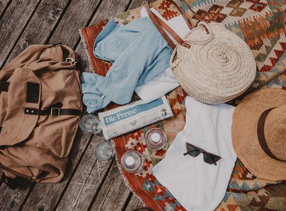 Ein gepackter Picknickplatz mit einer Decke und verschiedenen Gegenständen. Dazu gehören eine Tasche, ein Hut, Sonnenbrillen und Zeitungen.