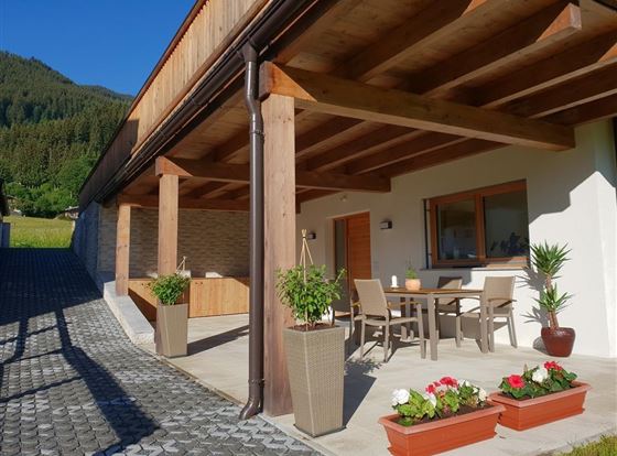 Eine moderne Terrasse mit einem Tisch und Stühlen, umgeben von Pflanzen. Im Hintergrund sind Berge und ein klarer Himmel zu sehen.