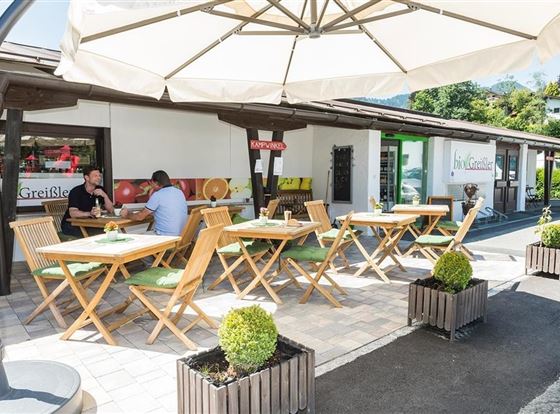Eine einladende Terrasse mit Holzmöbeln und Sonnenschirmen. Zwei Gäste genießen ihre Zeit in einem gemütlichen Außenbereich.