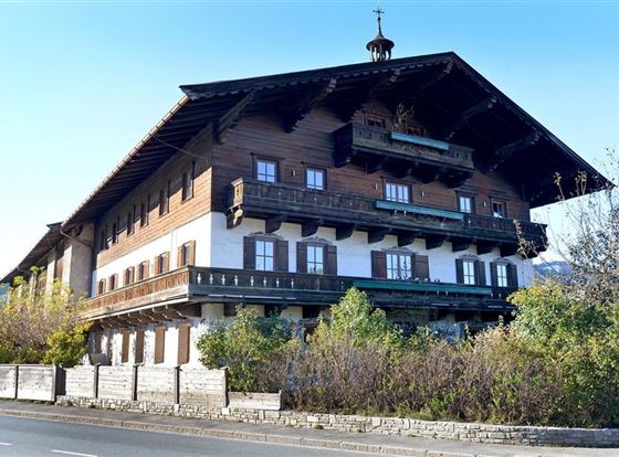 Ein traditionelles alpenländisches Holzhaus mit großen Balkonen. Das Gebäude ist von Bäumen und Sträuchern umgeben.