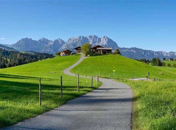 Eine malerische Landschaft mit grünen Wiesen und Bergen im Hintergrund. Ein ruhiger Weg führt zur historischen Anlage.