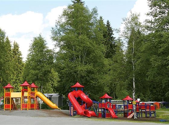 Ein bunt gestalteter Spielplatz mit Rutschen und Spielgerüsten. Umgeben von Bäumen und einer entspannten Landschaft.