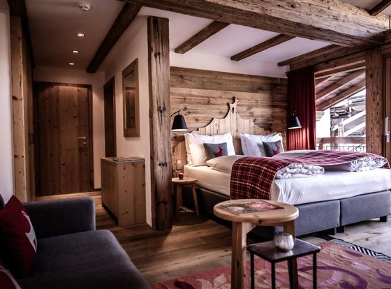 Ein gemütliches Schlafzimmer mit Holzverkleidung und einem großen Bett. Helle Fenster bieten einen Blick nach draußen und der Raum ist stilvoll mit modernen und rustikalen Elementen eingerichtet.