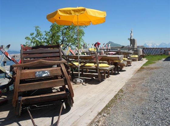 Ein sonniger Außenbereich mit Holzmöbeln und einem gelben Sonnenschirm. Entspannte Atmosphäre mit einer schönen Aussicht auf die Berge.