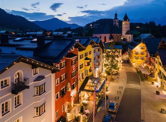 Eine malerische Straßenansicht bei Nacht mit bunten Häusern und einem Kirchturm im Hintergrund. Die sanfte Beleuchtung schafft eine einladende Atmosphäre.
