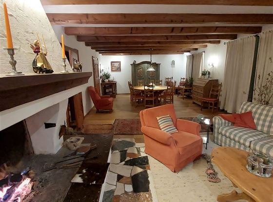 Ein gemütlicher Wohnraum mit Holzdecke und einem offenen Kamin. Rote Sessel und ein kariertes Sofa laden zum Entspannen ein.