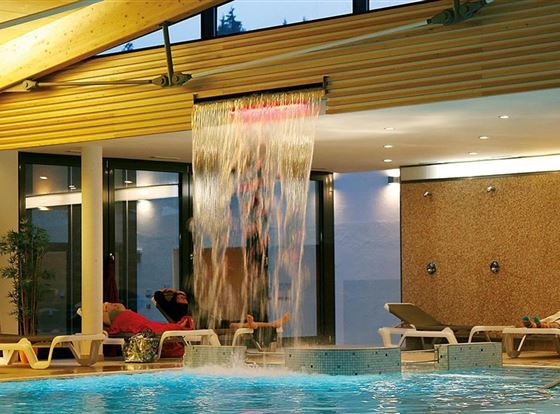 Ein entspannendes Hallenbad mit einem Wasserfall und Liegen zum Relaxen. Das Licht sorgt für eine angenehme Atmosphäre.