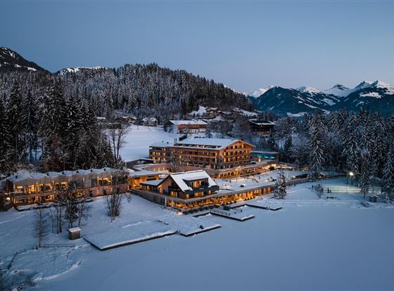 Ein malerisches Winterdorf, umgeben von schneebedeckten Bergen und Tannenbäumen. Die Gebäude sind sanft beleuchtet und reflektieren eine gemütliche Atmosphäre.