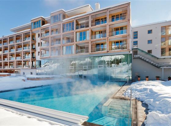 Ein modernes Hotel mit einem beheizten Außenpool, umgeben von Schnee. Der Pool dampft bei kaltem Wetter und sorgt für eine gemütliche Atmosphäre.