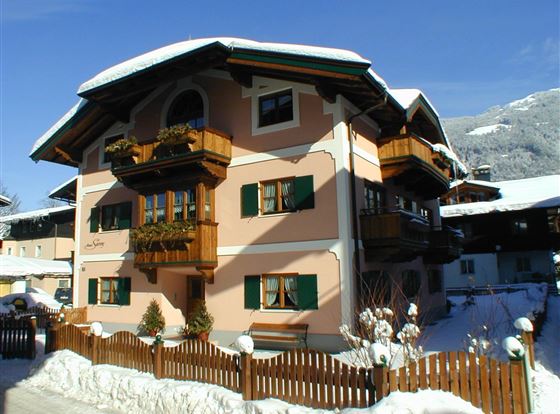 Ein charmantes, dreistöckiges Gebäude im alpinen Stil, umgeben von Schnee. Die bunten Fensterläden und Balkone verleihen dem Haus eine gemütliche Atmosphäre.
