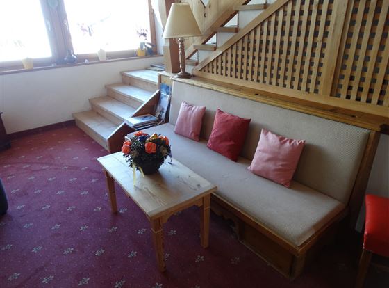 Ein gemütlicher Sitzbereich mit einem Holzsofa und bunten Kissen. Neben dem Sofa steht ein Tisch mit einer Blumendekoration.
