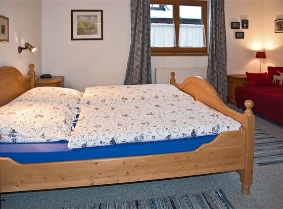 Ein gemütliches Schlafzimmer mit einem Doppelbett und einem Schlafsofa. Die Wände sind mit Bildern dekoriert und es gibt Fenster mit Vorhängen.