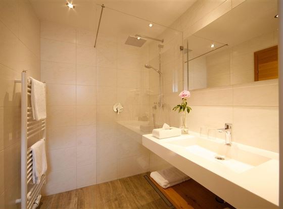 Ein modernes Badezimmer mit einer Glasdusche und einem eleganten Waschbecken. Weiße Fliesen und Holzdetails schaffen eine helle und einladende Atmosphäre.