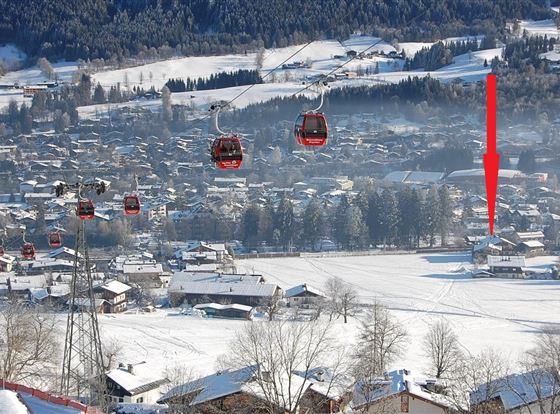 Eine schneebedeckte Landschaft mit mehreren Seilbahnen. Im Hintergrund sind ein kleines Dorf und verschneite Hügel zu sehen.