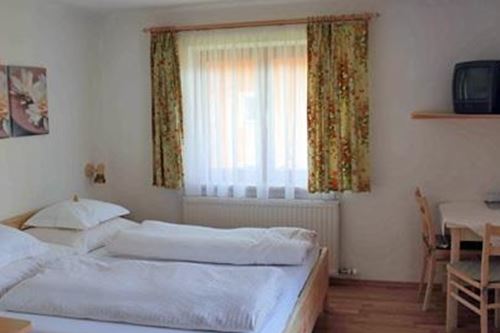 Ein helles Zimmer mit zwei Einzelbetten und einem Schreibtisch. Vor einem Fenster hängt ein Vorhang mit floralen Mustern.