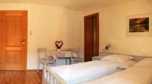 Ein gemütliches Zimmer mit zwei Einzelbetten und hellen Wänden. Es gibt eine Holzfußboden und eine kleine Sitzecke mit einem Tisch.