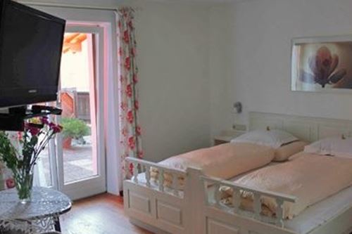 Ein gemütliches Schlafzimmer mit einem Doppelbett und einem Fernseher. Durch die Fenster gelangt viel Licht und es gibt einen kleinen Balkon.