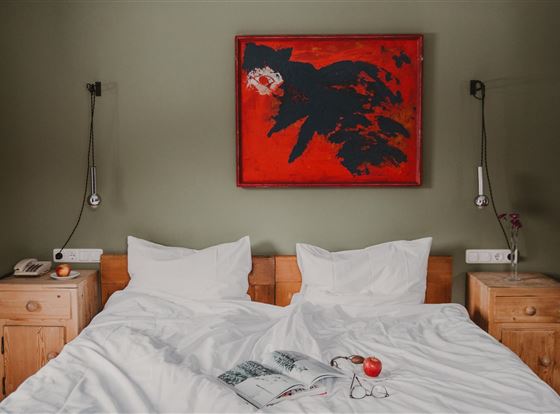 Ein modernes Schlafzimmer mit einem großen Bett und zwei Nachttischen. An der Wand hängt ein auffälliges rotes Gemälde.