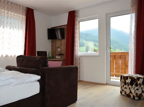 Ein gemütliches Zimmer mit einem Sofa und einem Bett. Große Fenster bieten einen Blick auf die grüne Landschaft.