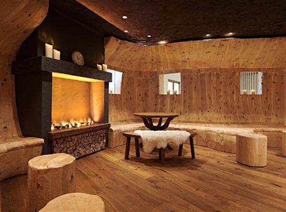 A cozy room with wooden paneling and a fireplace. There are round seating areas and a table in the middle.