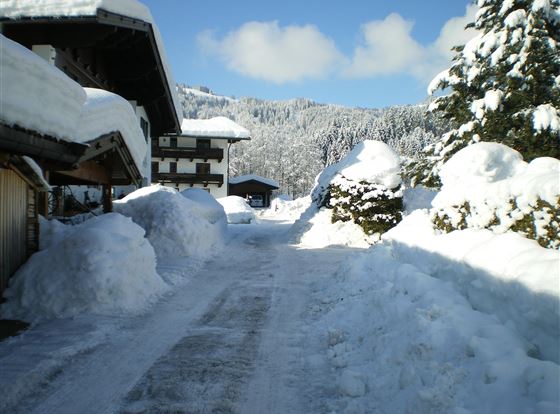 Eine verschneite Straße zwischen traditionellen Häusern. Im Hintergrund sind schneebedeckte Berge zu sehen.