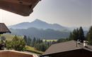 Eine malerische Berglandschaft mit sanften Hügeln und Bäumen. Im Hintergrund erheben sich majestätische Berge unter einem klaren Himmel.