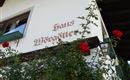 Ein altes Gebäude mit der Aufschrift "Haus Möggötter". Rote Rosen ranken an der Wand und verleihen dem Bild einen charmanten Charakter.