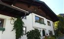 Ein traditionelles Haus mit einem Holzdach und grünen Fensterrahmen. Vor dem Haus sind Pflanzen und ein gepflegter Garten zu sehen.