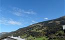 Eine malerische Landschaft mit grünen Hügeln und dichten Wäldern. Der Himmel ist klar und blau, mit wenigen Wolken.