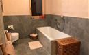 Ein modernes Badezimmer mit einer Badewanne und einer Dusche. Die Wände sind in sanften Farbtönen gehalten und der Boden besteht aus grauen Fliesen.