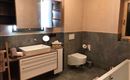 Ein modernes Badezimmer mit einer Badewanne, einem Waschbecken und einem großen Spiegel. Die Wände sind in sanften Farben gehalten und es gibt praktische Ablageflächen.