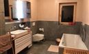 Ein modernes Badezimmer mit einer Badewanne und einem Waschbecken. Die Wände sind in sanften Farben gehalten und es gibt eine große Spiegelfläche.