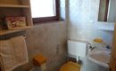 Ein kleines Badezimmer mit hellen Fliesen. Es enthält eine Toilette mit einem gelben Deckel und ein Waschbecken.