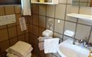 Ein kleines Badezimmer mit braunen Fliesen. Es sind Handtücher, ein Waschbecken und ein Toilettenbereich sichtbar.