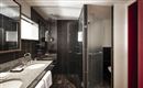 A modern bathroom with dark tiles and two sinks. The shower is glass and the room is well lit.