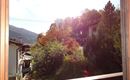 Ein Blick aus einem Fenster auf eine bunte Herbstlandschaft. Bäume und Häuser sind von warmem Licht beleuchtet.