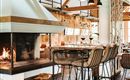 A modern restaurant with an inviting fireplace and stylish bar stools. The space is brightly and cozily designed.