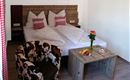 Ein gemütliches Schlafzimmer mit einem Doppelbett und gepolsterten Kissen. Neben dem Bett steht ein Tisch mit frischem Obst und einer Vase mit einer Blume.