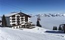 Ein schneebedecktes Bergpanorama mit einem gemütlichen Hotel und einer Seilbahn. Die Aussicht zeigt die beeindruckenden Berge und einen wolkenverhangenen Himmel.