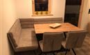 Ein modernes Esszimmer mit einer U-förmigen Bank und einem Holztisch. Die warmen Farben und das gemütliche Ambiente laden zum Verweilen ein.
