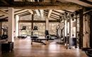 Ein moderner Fitnessraum mit Holzverkleidung und großen Fenstern. Es sind verschiedene Fitnessgeräte wie Laufbänder und Hantelstationen vorhanden.