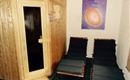 Ein gemütlicher Wellnessbereich mit einer Sauna und zwei Liegen. Die Wände sind aus Holz und ein farbiges Bild hängt an der Wand.