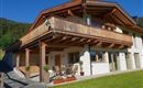 Ein modernes Haus mit Holzverkleidung und großem Balkon. Der schöne Außenbereich enthält einen Garten mit Pflanzen und Sitzgelegenheiten.