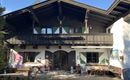 Ein traditionelles Alpenhaus mit einem schönen Balkon und bunten Fenstern. Der Außenbereich ist mit Stühlen und Tischen zum Entspannen ausgestattet.