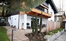 Ein modernes Haus mit einem großzügigen Balkon und einer gemütlichen Terrasse. Der Garten ist gepflegt und mit Steinen und Pflanzen gestaltet.
