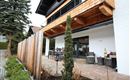 Eine moderne Terrasse mit einem Garten und einem Holzsichtschutz. Im Hintergrund ist ein gemütlicher Tisch und Stühle zu sehen.