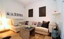 Ein gemütliches Wohnzimmer mit einem großen beigen Sofa und bunten Kissen. Neben dem Sofa steht ein Holztisch und an der Wand hängen einige Bilder.