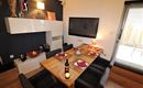 Ein modernes Esszimmer mit einem großen Holztisch und stilvollen Stühlen. Die Wände sind dunkel, und ein Fernseher hängt über dem Tisch.