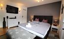 Ein stilvolles Schlafzimmer mit einem großen Doppelbett und gemütlichen Kissen. Die Wände sind in neutralen Tönen gehalten, und es gibt modernes Licht und Dekorationen.